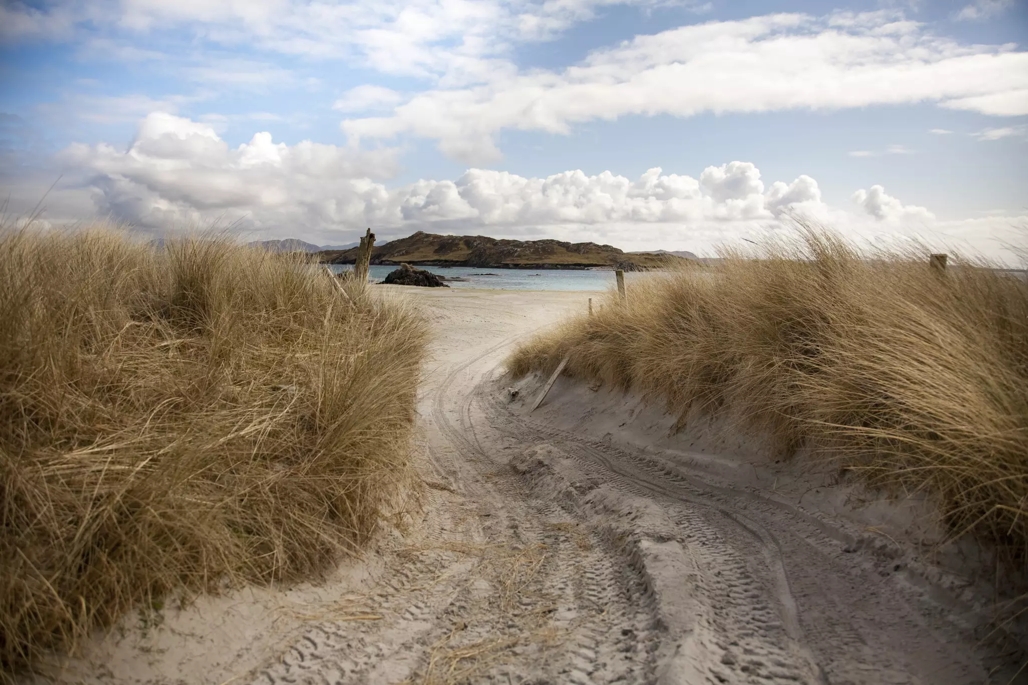 A sandy path leads through grasses toward the beach and water on Inishbofin island, Connemara, Ireland