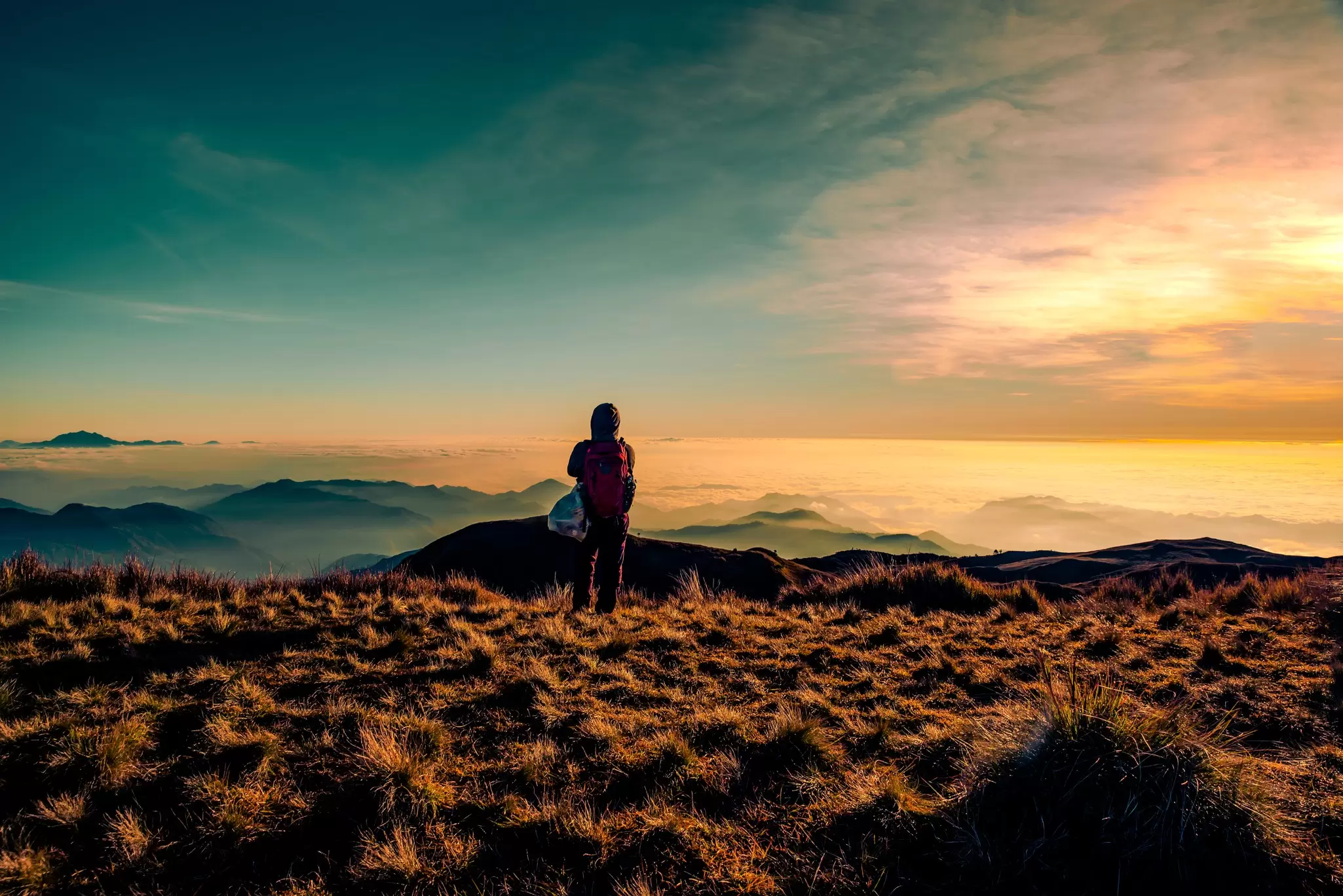 An adult mountainer standing at the peak of Mt. Pulag enjoying the breathtaking view of sea of clouds during sunrise.