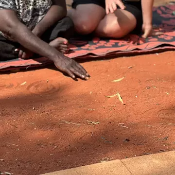An Anangu artist from Maruku demonstrates symbology in traditional artwork at Yulara Town Square. Northern Territory, Australia.