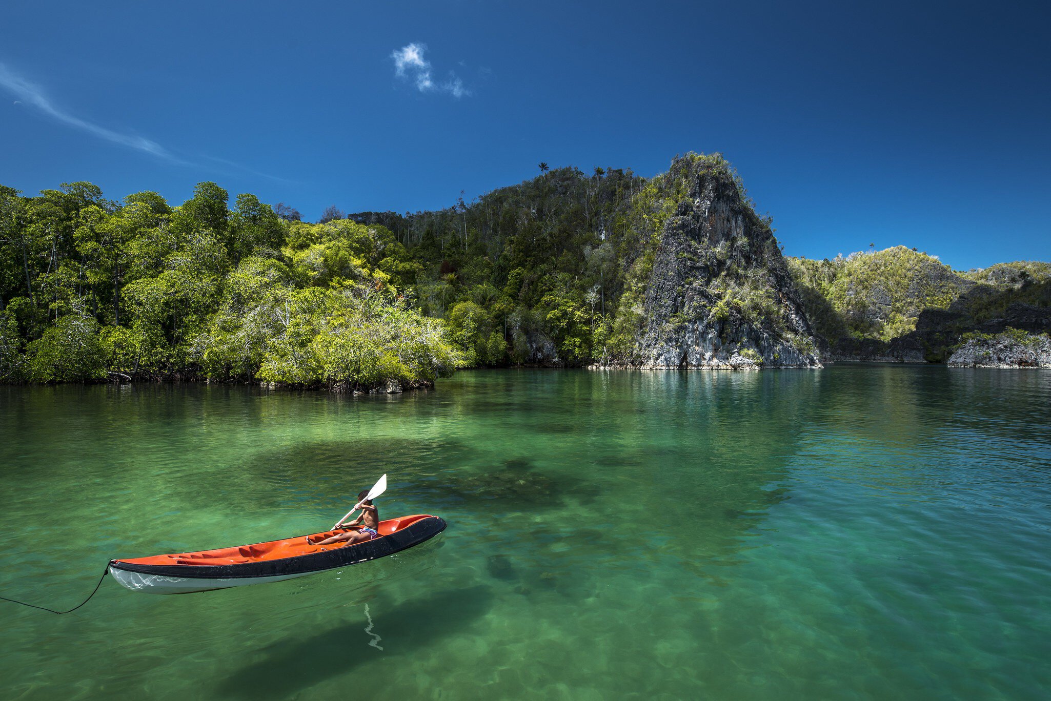 Young boy canoeing through clear water in Raja Ampat. 