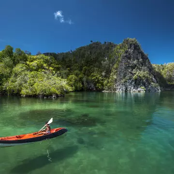 Young boy canoeing through clear water in Raja Ampat. 