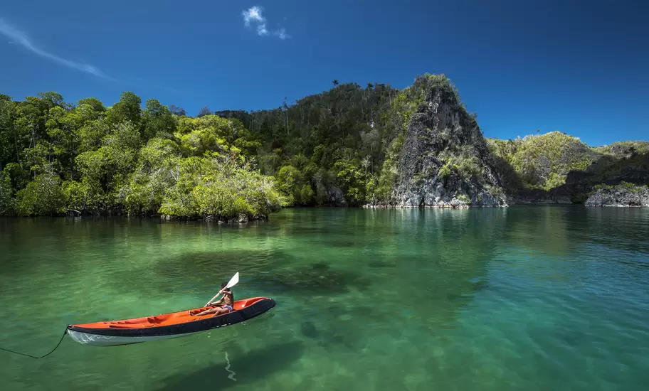 Young boy canoeing through clear water in Raja Ampat. 
