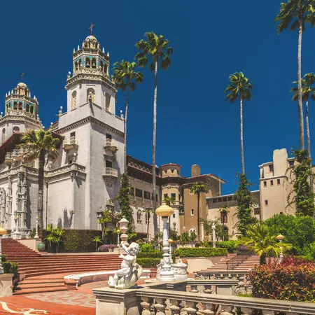 Exterior view of an elaborate residential castle, with baroque-style towers, with palm trees on the plaza