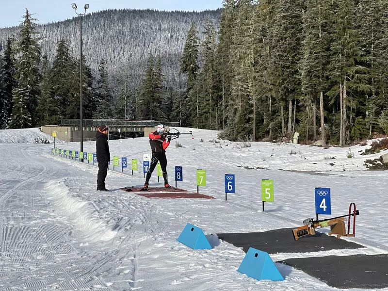 An athlete armed with a rifle takes aim towards a target during training
