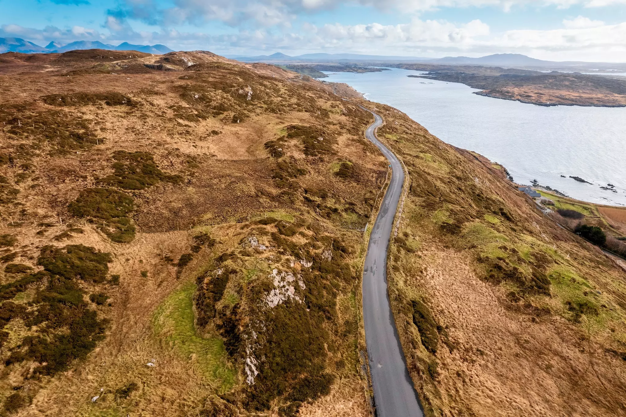 An aerial view of a paved road along a hillside overlooking an inlet below, Connemara, Ireland