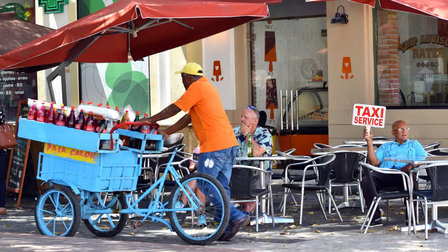 A taxi driver looking for passengers while a drinks cart passes in Santo Domingo, Dominican Republic