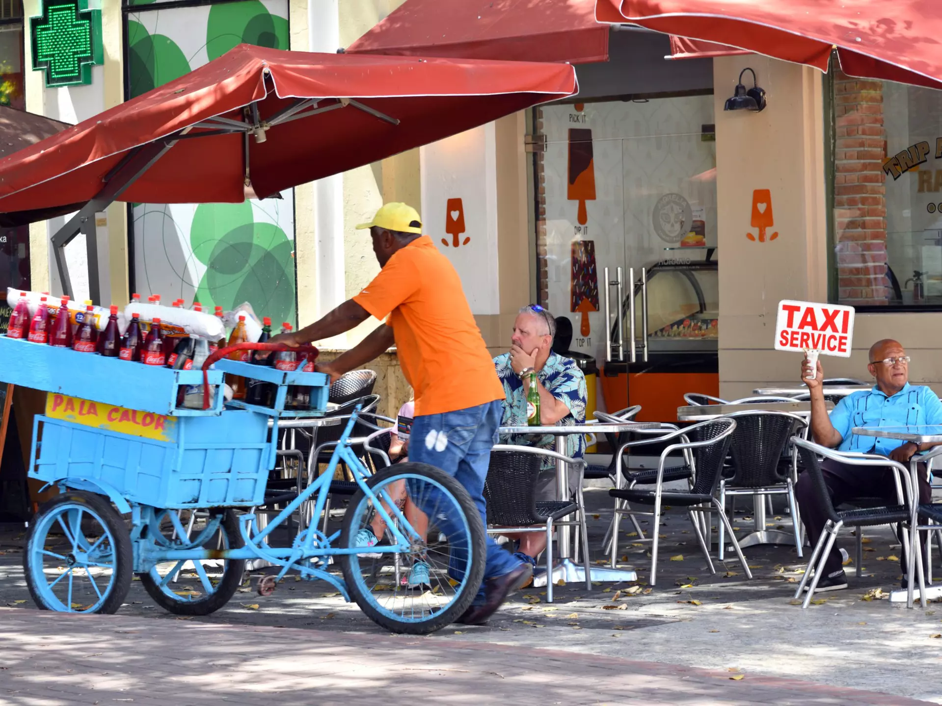 A taxi driver looking for passengers while a drinks cart passes in Santo Domingo, Dominican Republic