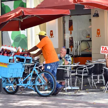 A taxi driver looking for passengers while a drinks cart passes in Santo Domingo, Dominican Republic