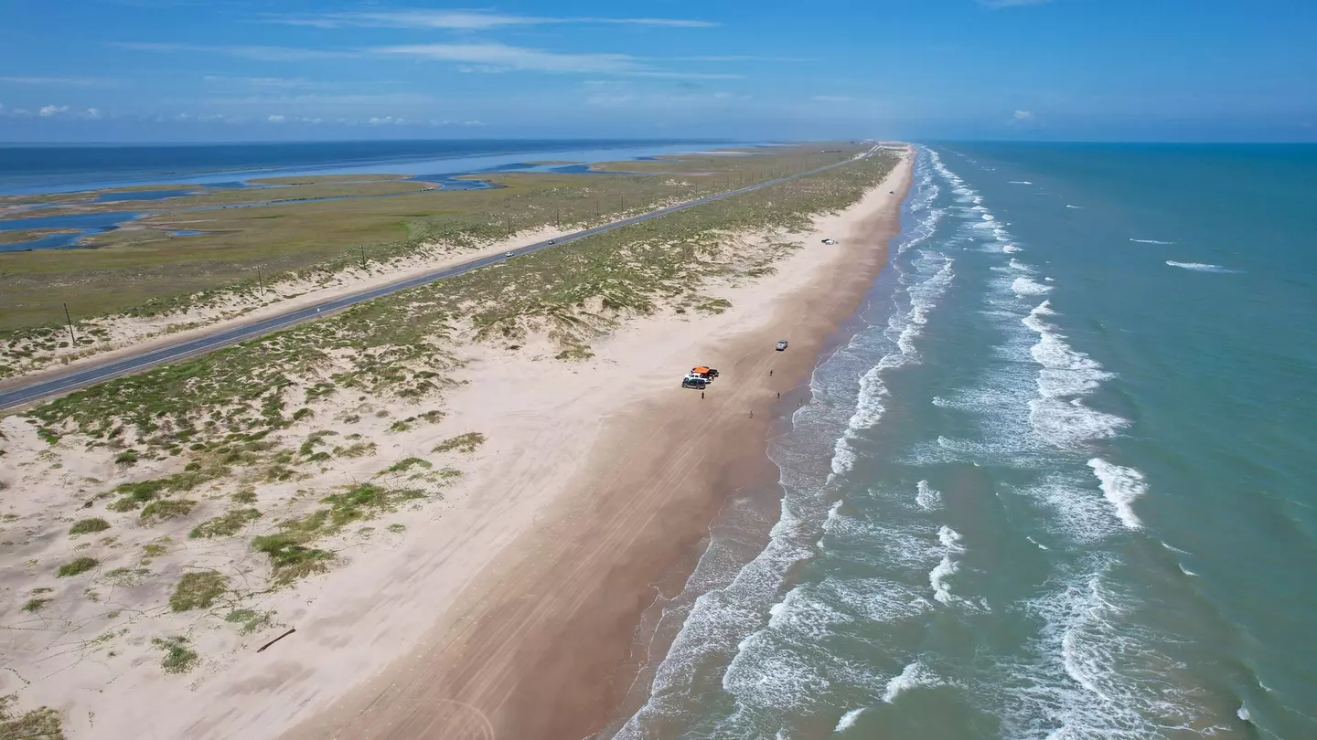 An aerial view of a near-deserted beach on a long barrier island by the sea.