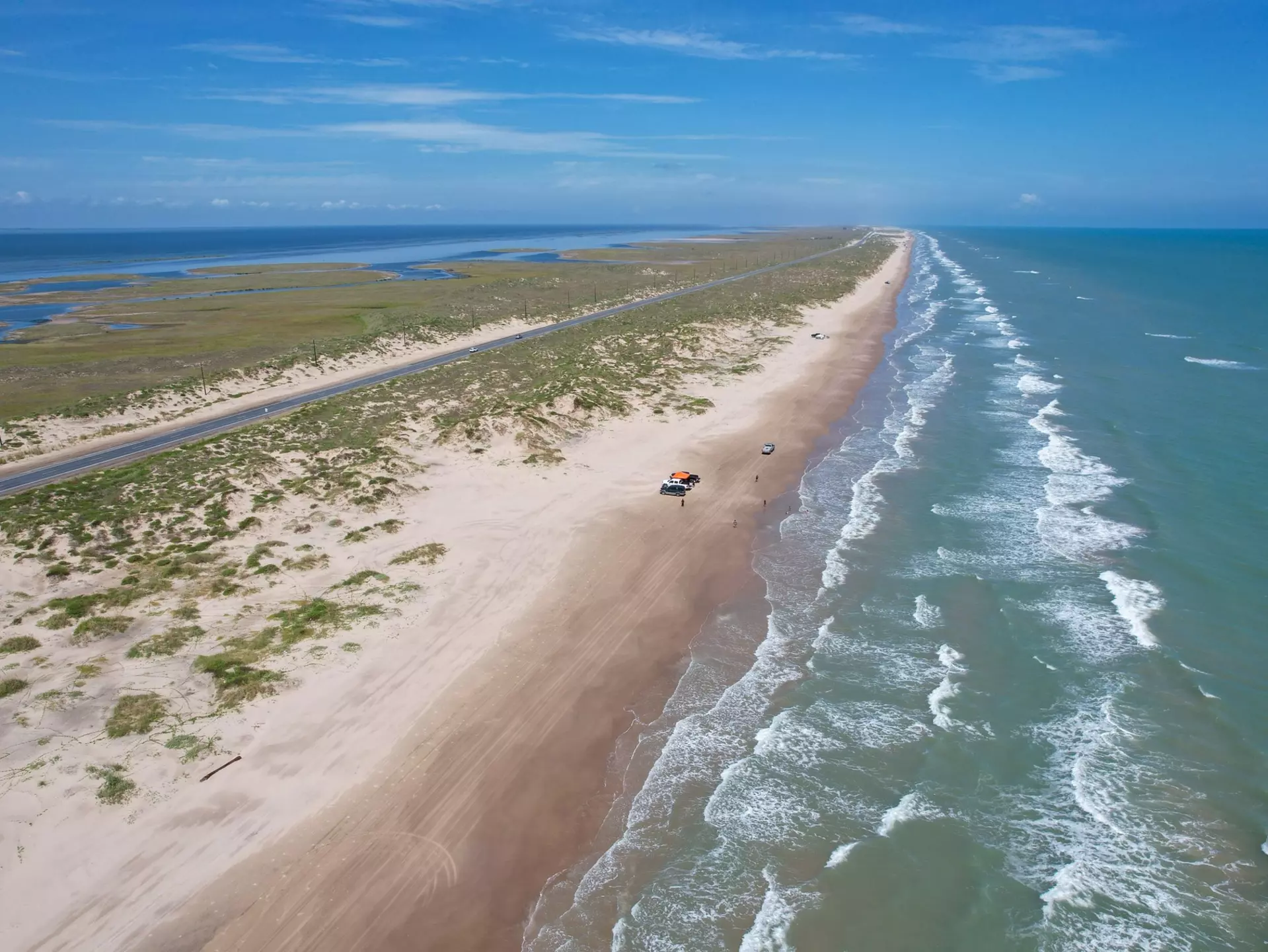 An aerial view of a near-deserted beach on a long barrier island by the sea.