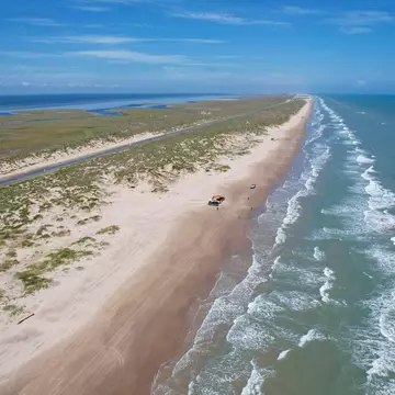 An aerial view of a near-deserted beach on a long barrier island by the sea.