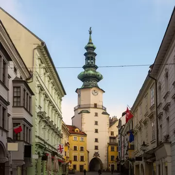 Green copper spire of Michael's Gate tower rising at the end of a narrow street of pastel buildings in Bratislava