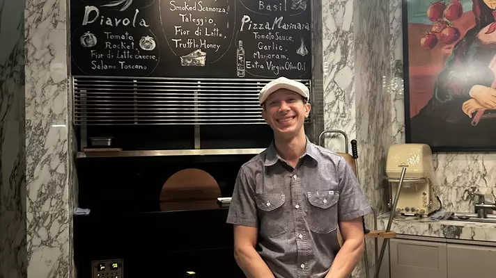 A pizzaiolo (pizza maker) smiles for a photo in front of his pizza oven