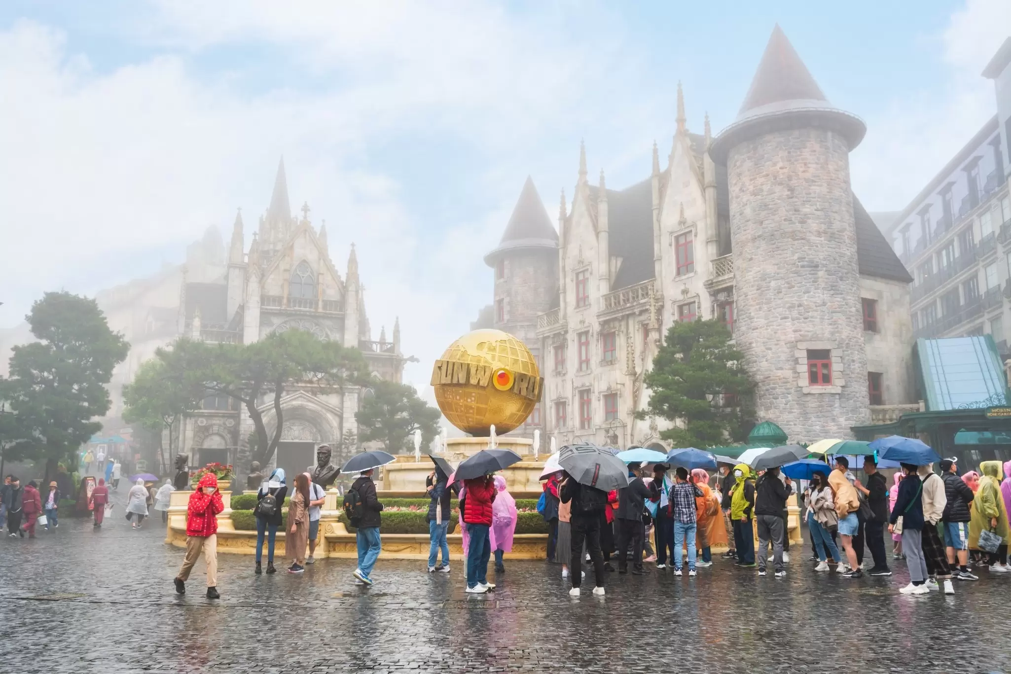 People hold umbrellas in stormy, misty conditions at a theme park with fairy-tale-style buildings, Danang, Vietnam