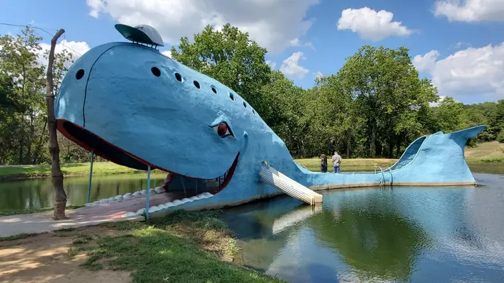 A fiberglass, cartoon-like depiction of a blue whale sits in a pond.