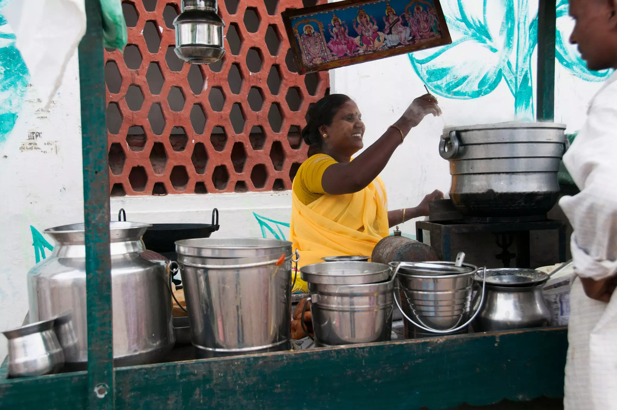 A woman running a roadside food stall stirs something in a large stainless steel pot