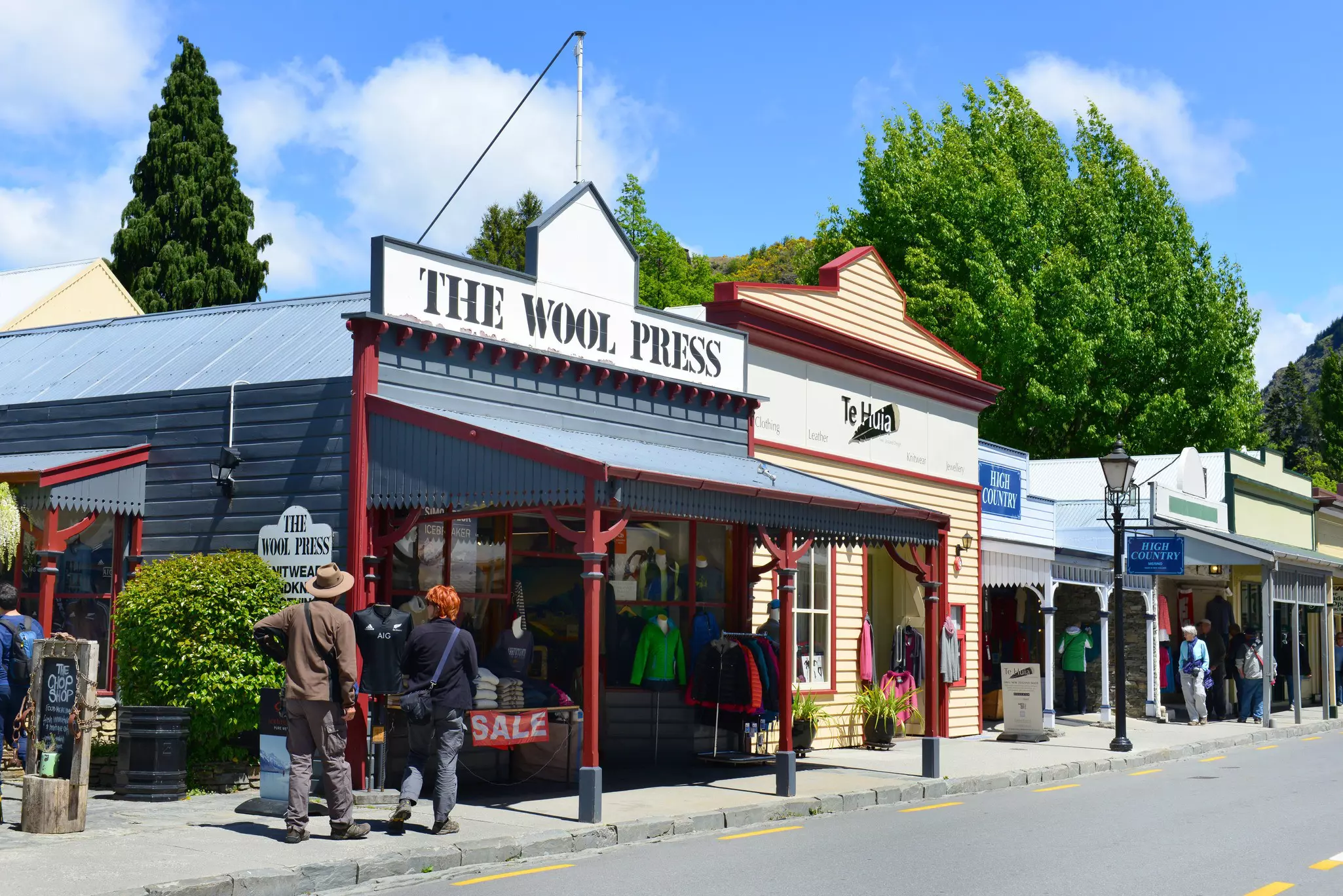 Nineteenth-century storefronts lining a street. Shoppers browse the shop windows.