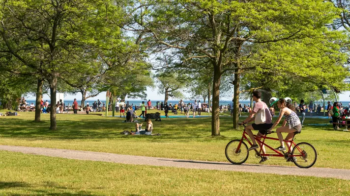 People riding a tandem bike through a busy green park 