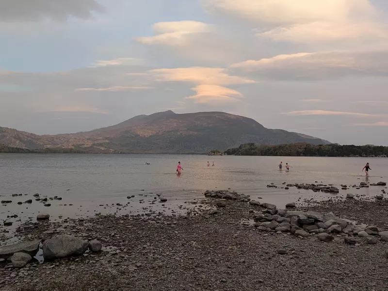 People in the water off a rocky beach at sunrise.