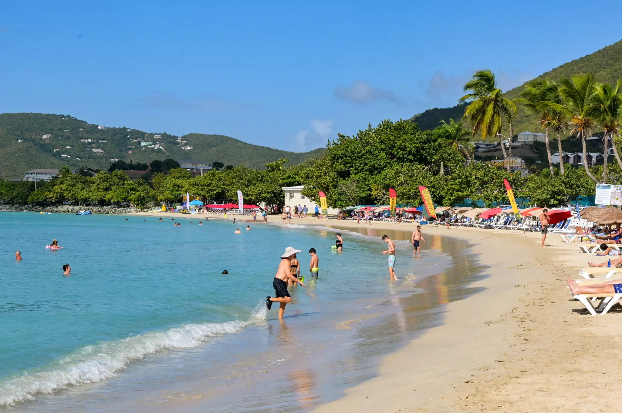People and swimming in the ocean and relaxing on a beach lined with sunloungers and resorts.