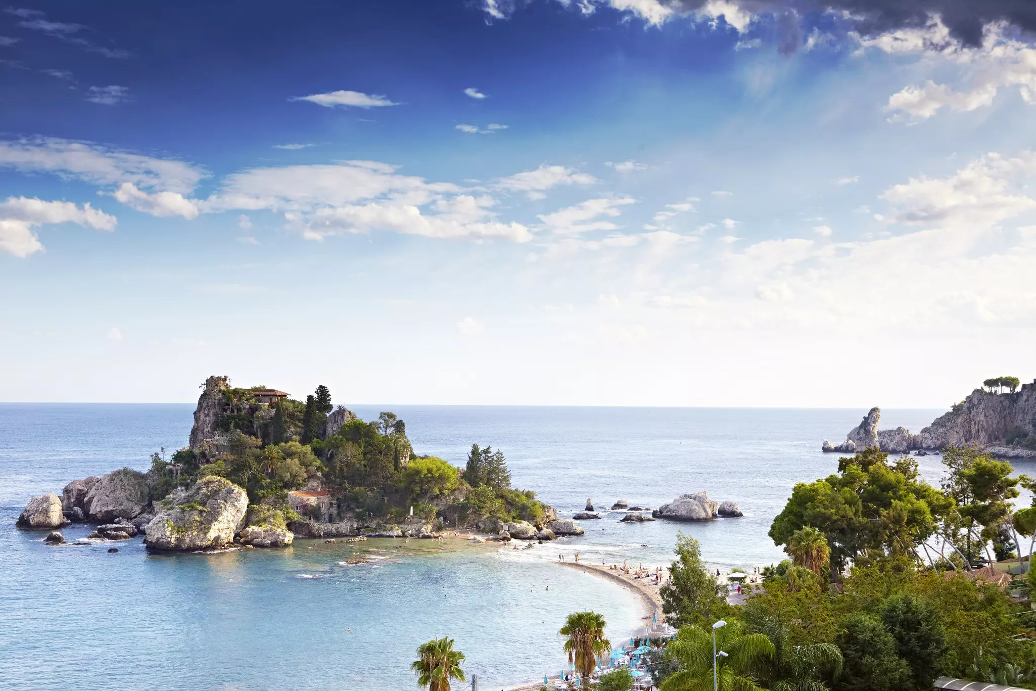 A small, rocky island with a narrow, sandy path leading toward it on a sunny day.
