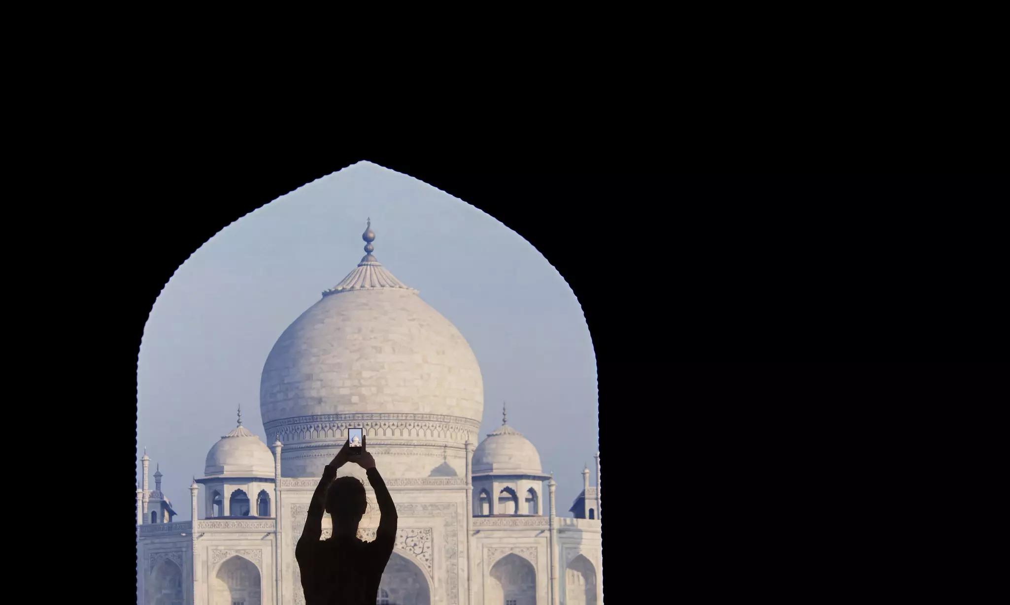 Female tourist taking photograph form entrance of the Taj Mahal in morning light