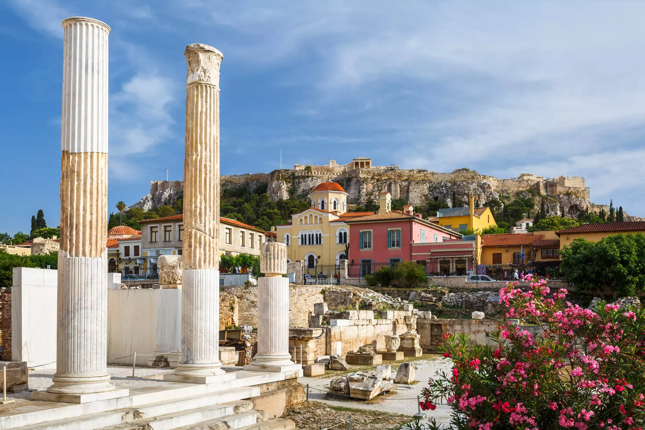 Stone columns with brightly colored homes and ruins on a hillside beyond on a sunny day.