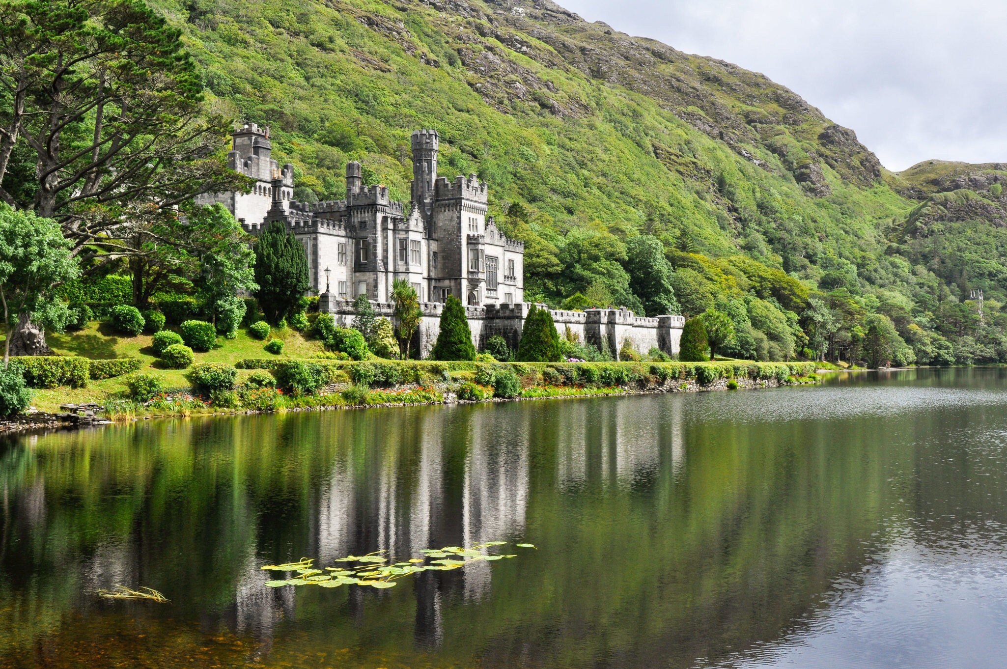 Exterior and reflection of Kylemore Abbey, in Galway, Ireland. Surrounded by lush greenery and water.