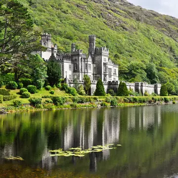 Exterior and reflection of Kylemore Abbey, in Galway, Ireland. Surrounded by lush greenery and water.