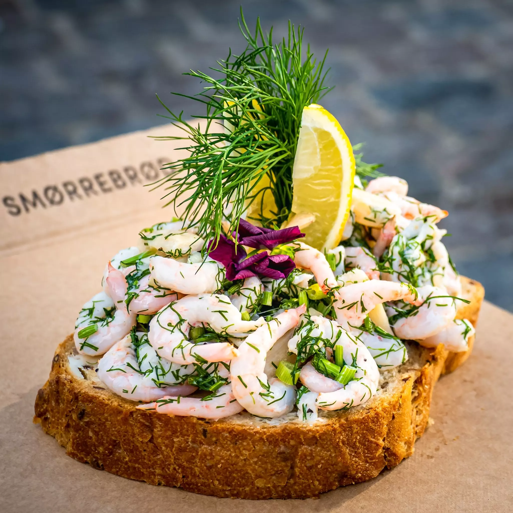 An open-faced sandwich is piled high with shrimp, dill and other toppings.