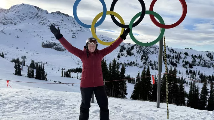 A woman in ski geat stands in front of the iconic five-ring design of the Olympic Games