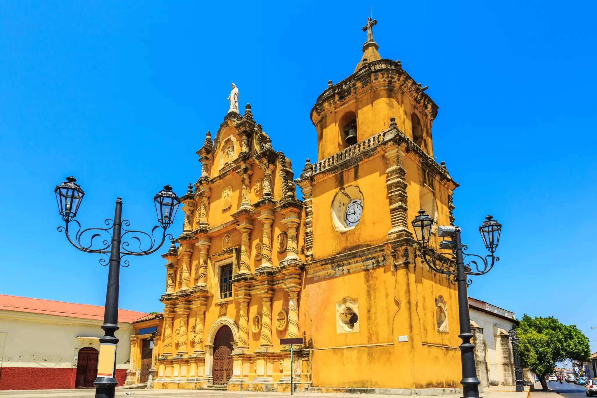 A baroque-style bright yellow church on a corner in the city of León. In front there are a pair of gothic-styled light posts; Nicaragua travel.