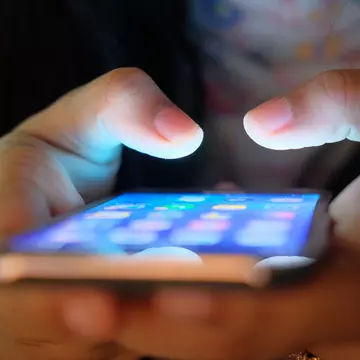 The menu of a smartphone is visible as the phone is held in a hand