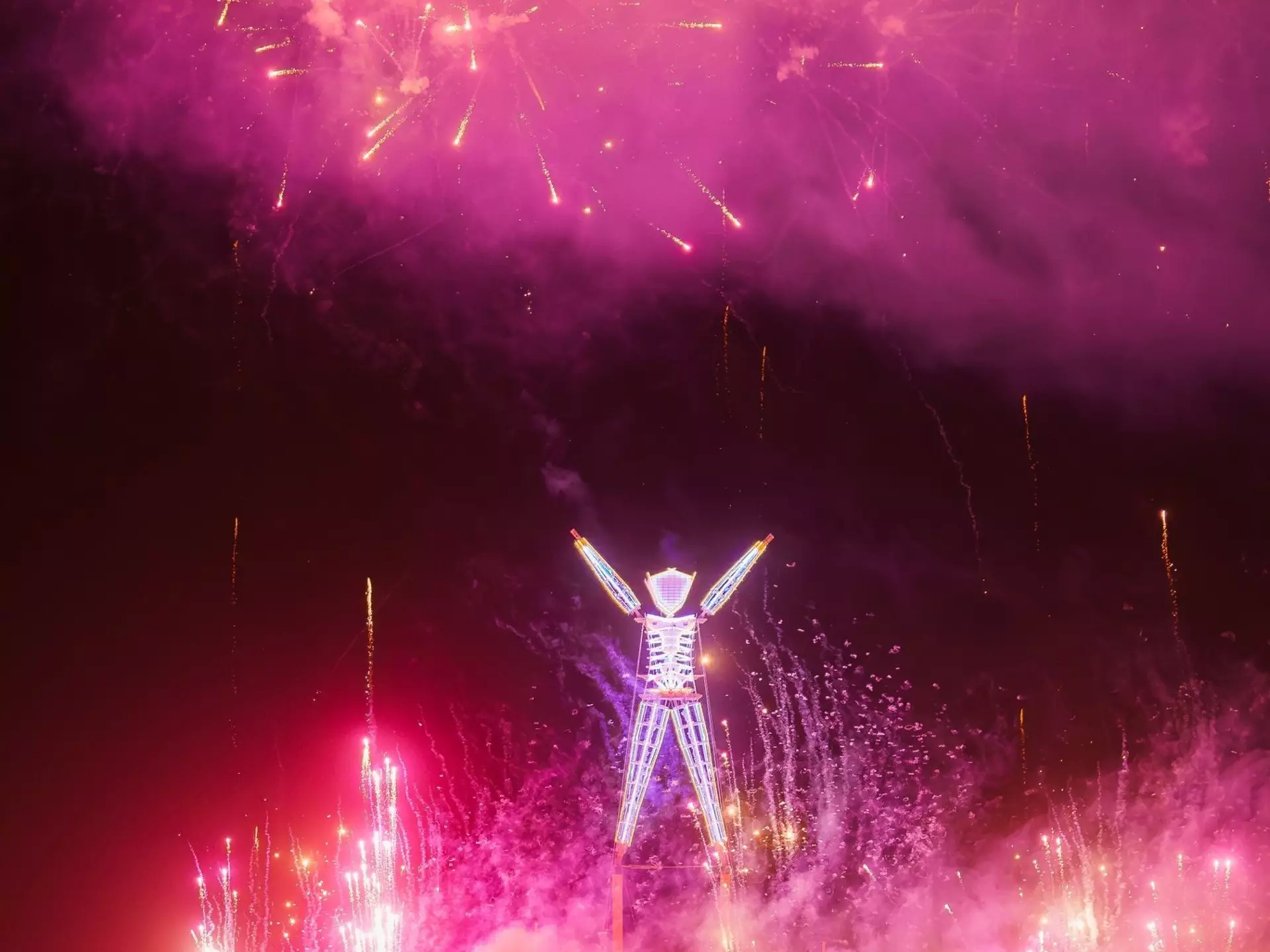 A large, glowing effigy surrounded by fireworks and silhouetted participants