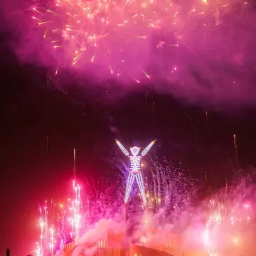 A large, glowing effigy surrounded by fireworks and silhouetted participants