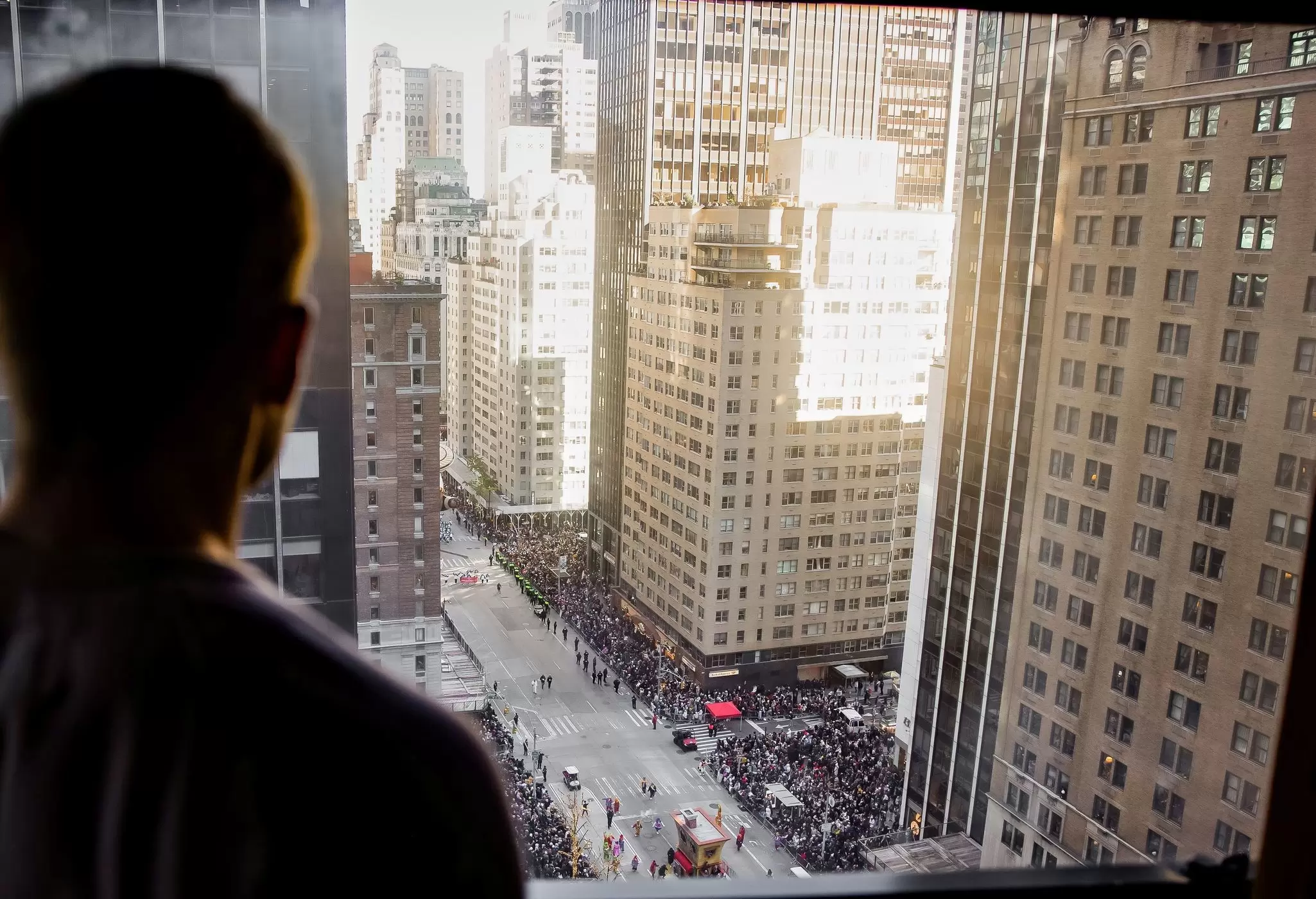 A man watches a parade on a city street below his hotel room: A room at New York Hilton Midtown