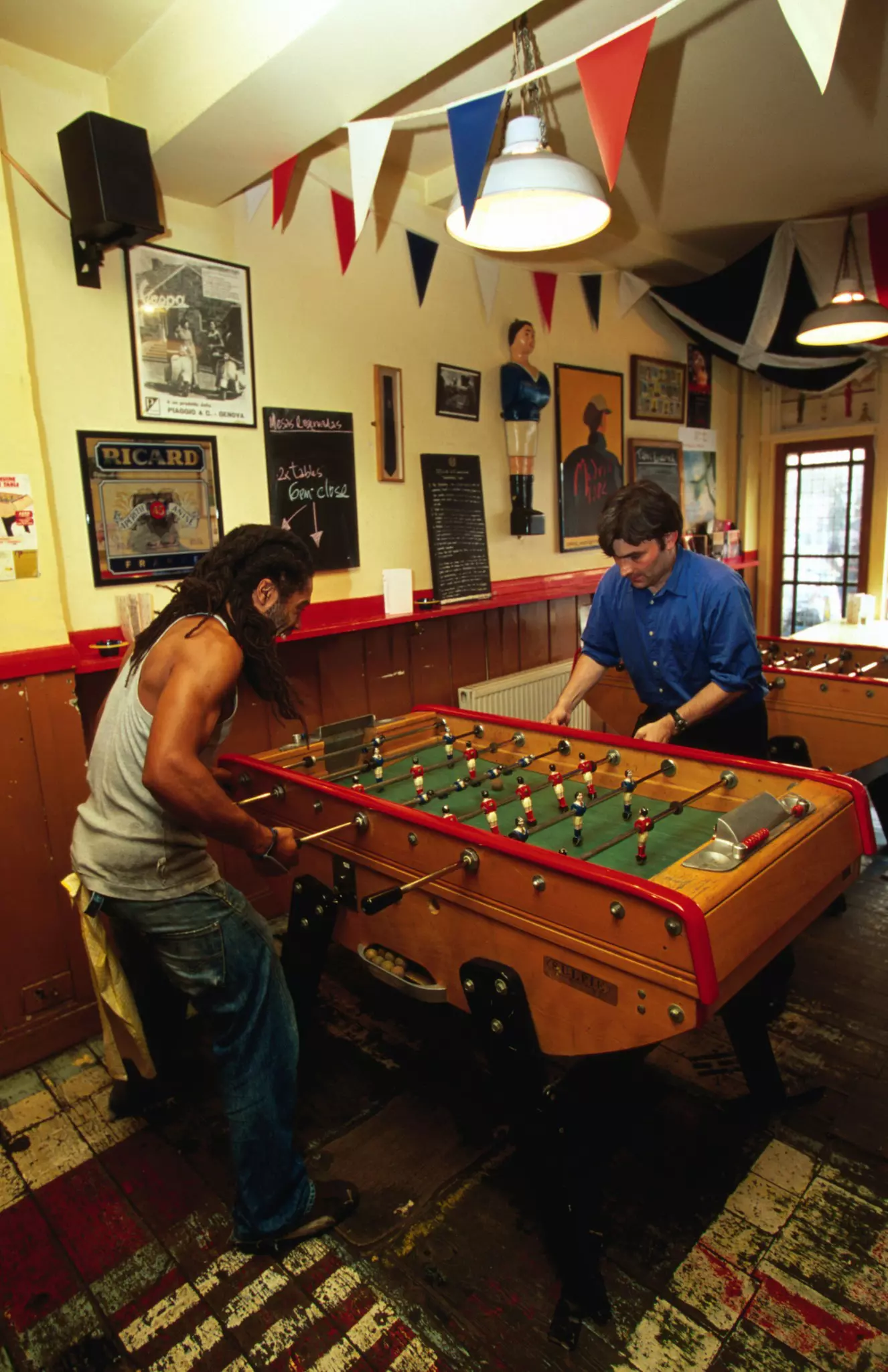 The exterior of Cafe Kick sports Bar in Exmouth Market. There is a branch of a cherry blossom in the foreground, slightly obscuring the cafe which has lots of outdoor seating