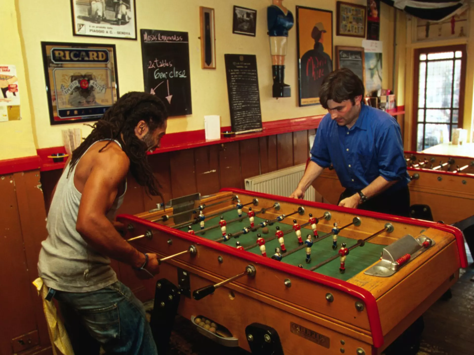 The exterior of Cafe Kick sports Bar in Exmouth Market. There is a branch of a cherry blossom in the foreground, slightly obscuring the cafe which has lots of outdoor seating