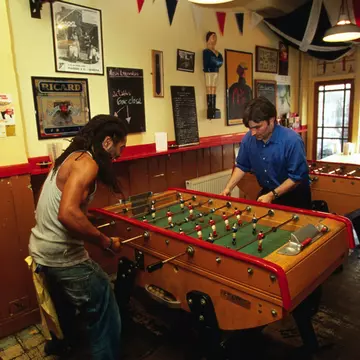 The exterior of Cafe Kick sports Bar in Exmouth Market. There is a branch of a cherry blossom in the foreground, slightly obscuring the cafe which has lots of outdoor seating