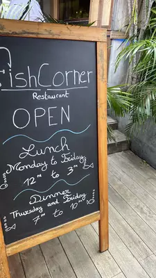 A chalkboard placard for Fish Corner restaurant with its hours on it
