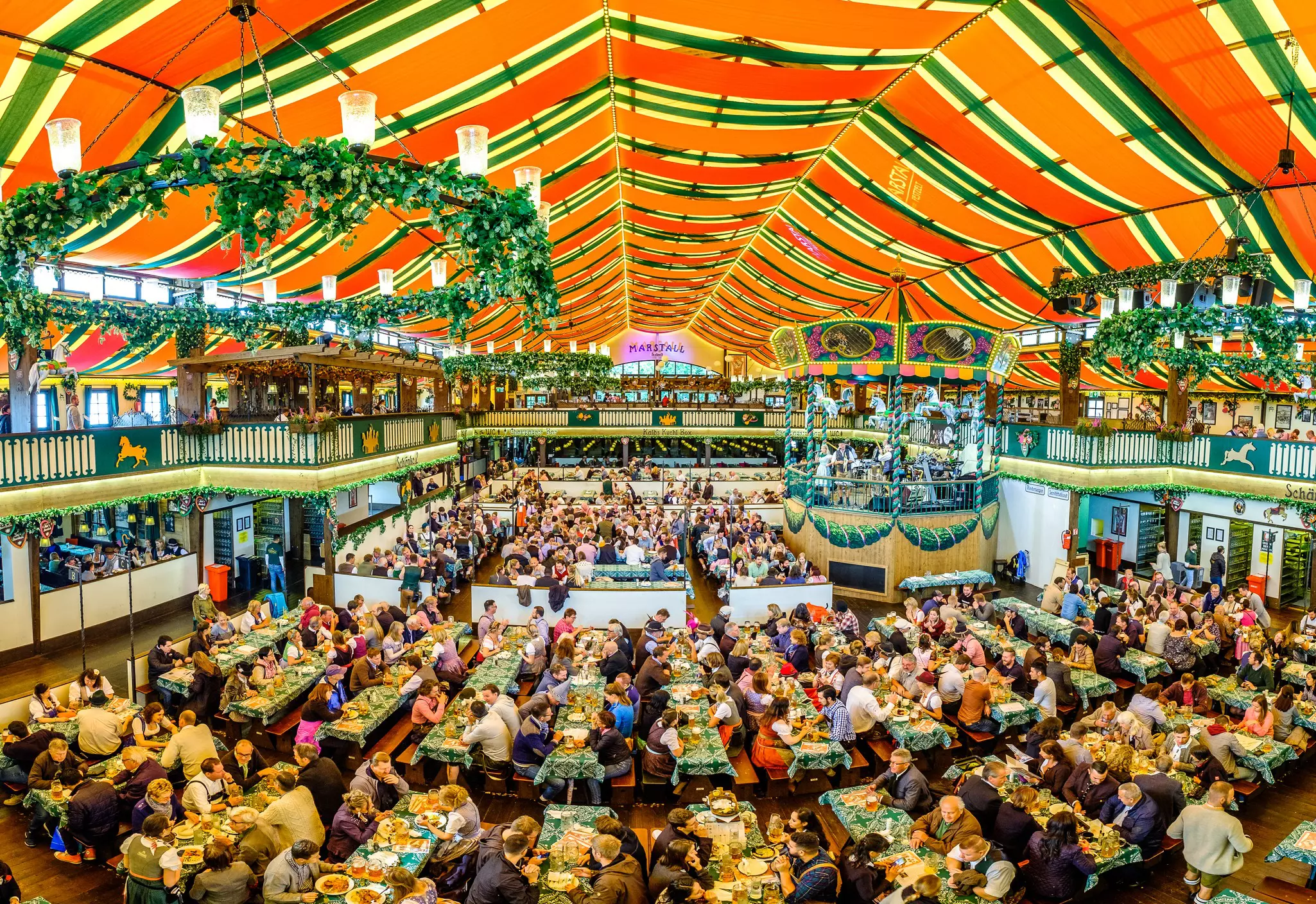 People crowded at tables eating food and drinking beer in a massive festival tent.