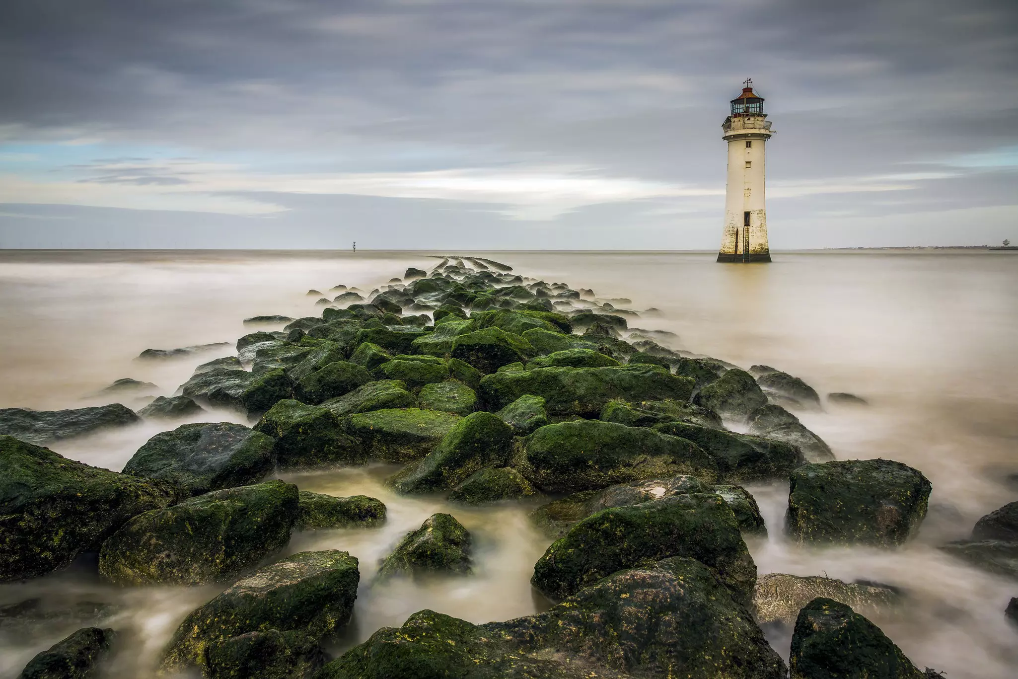 View of New Brighton Lighthouse with mossy rocks on the beach in the foreground