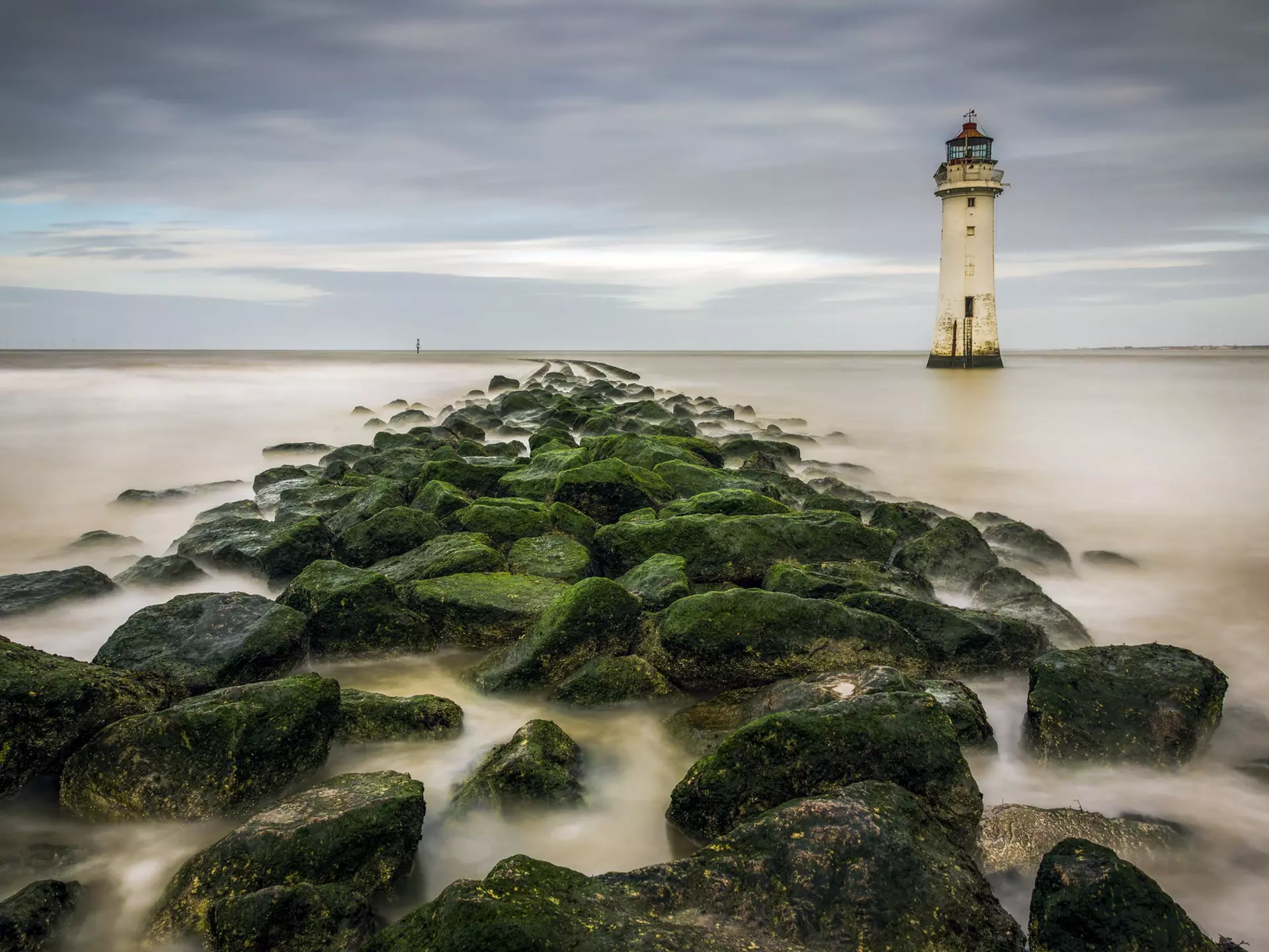 View of New Brighton Lighthouse with mossy rocks on the beach in the foreground