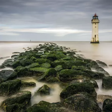 View of New Brighton Lighthouse with mossy rocks on the beach in the foreground