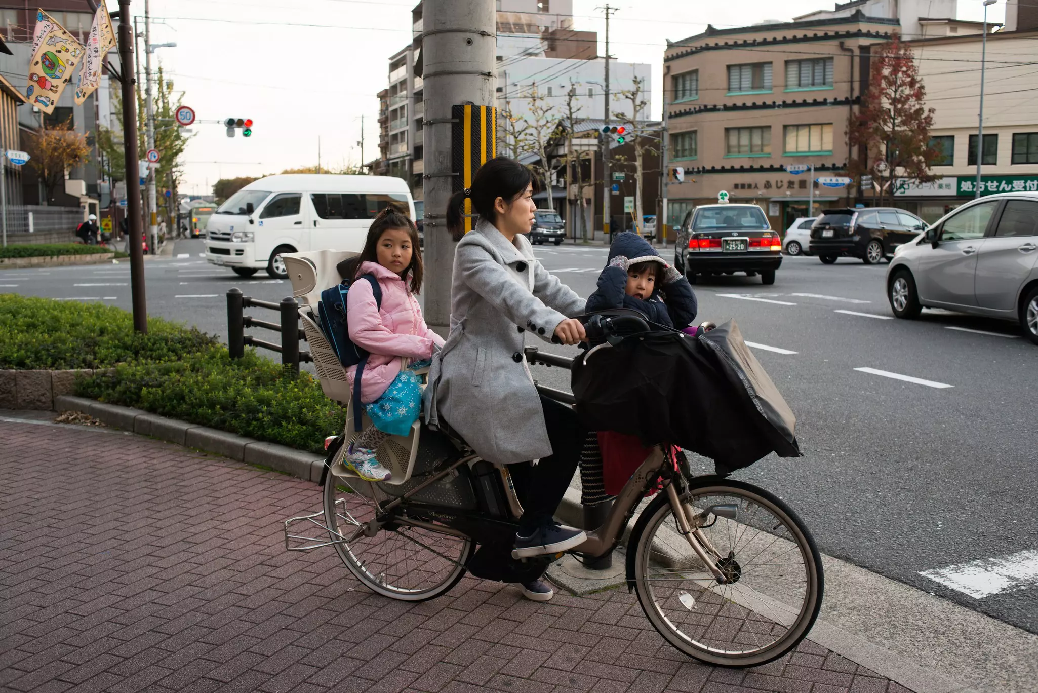 A woman with two children in seats on her bicycles stops at a red light on a city street.