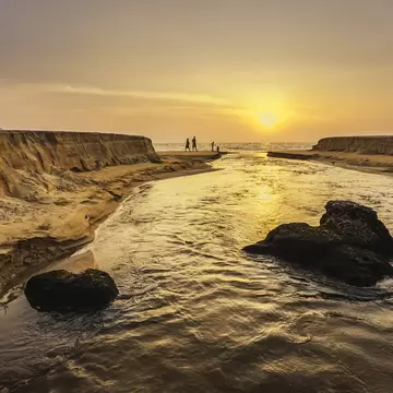 Kannur, Kerala, India. Sunset as Thottada river carves a channel through the sandy beach at Thottada village and spills into Arabian Sea, north Kerala, India.