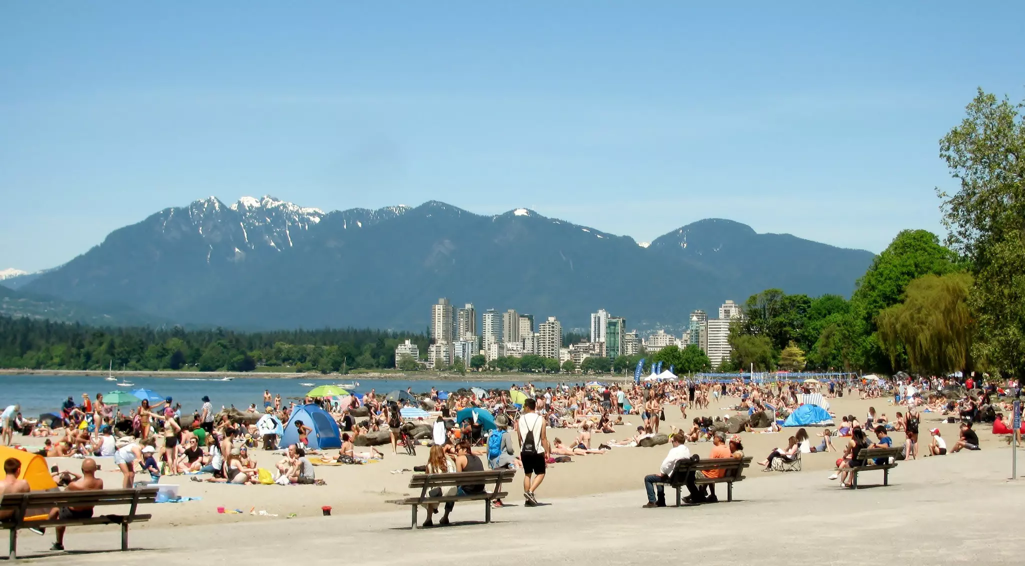 People enjoy a beach on a sunny day with mountains in the background.