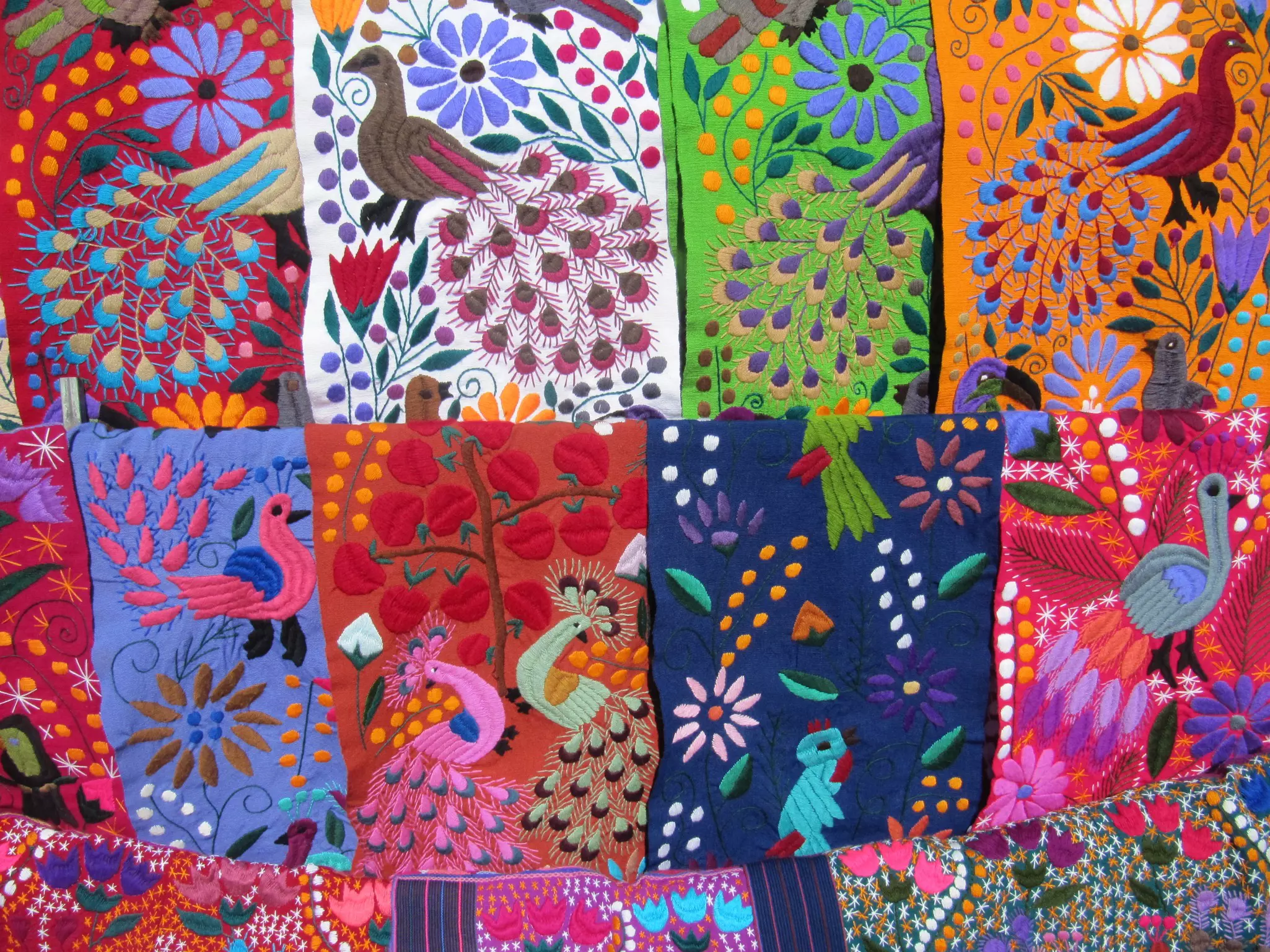 Colorful woven cloth in pinks, purples, greens, and blue, with images of peacocks and flowers.