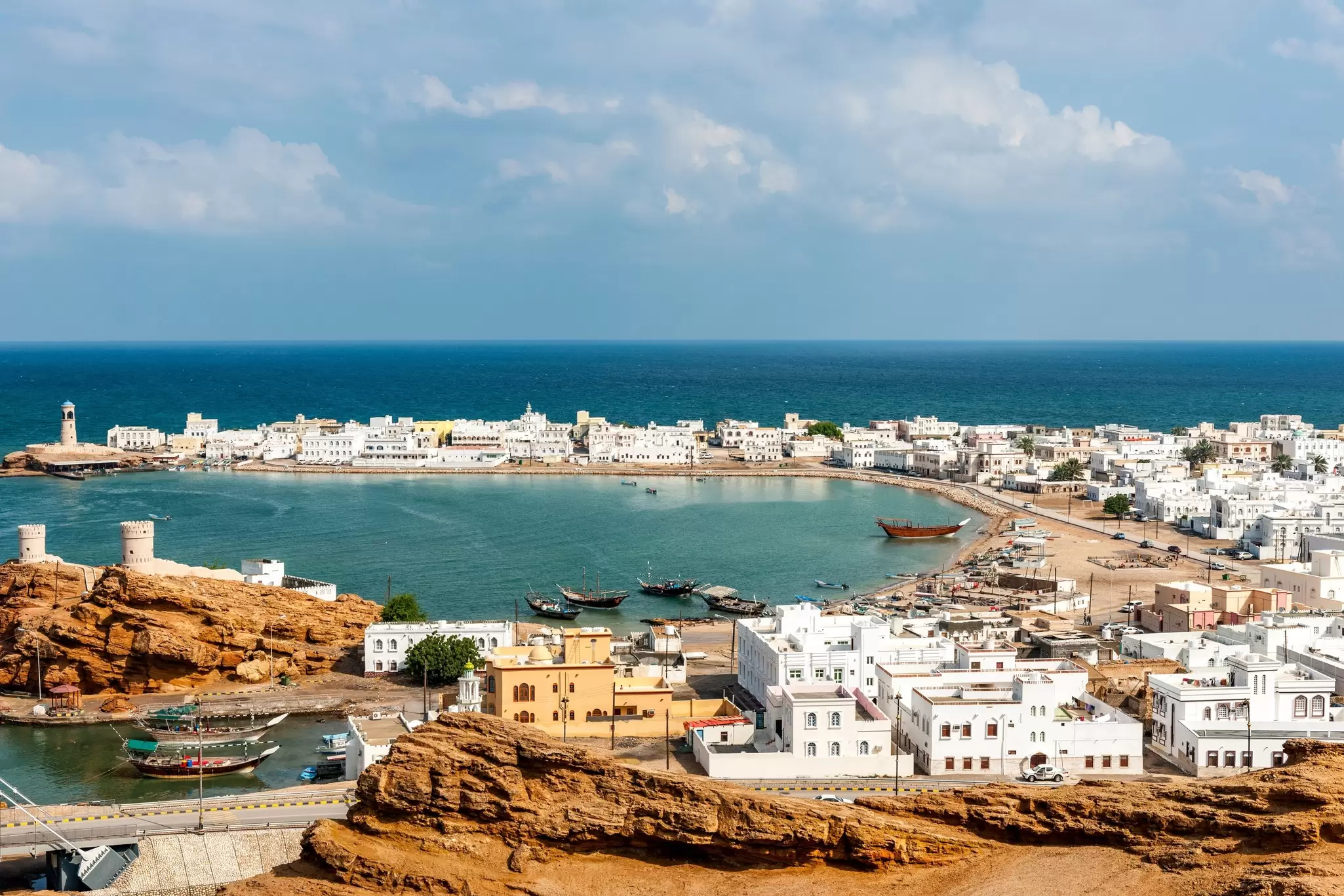 A fishing village with traditional wooden dhows docked in the harbor surrounded by low-rise white buildings; Sur, Oman.
