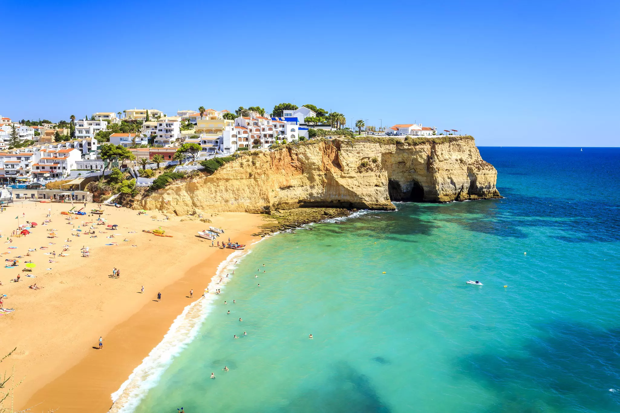 A sandy beach with cliffs at one end an small houses and resorts build on the hillside.